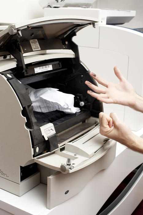 Cropped view image of a man shaking his fists in frustration at a photocopier with a paper jam
