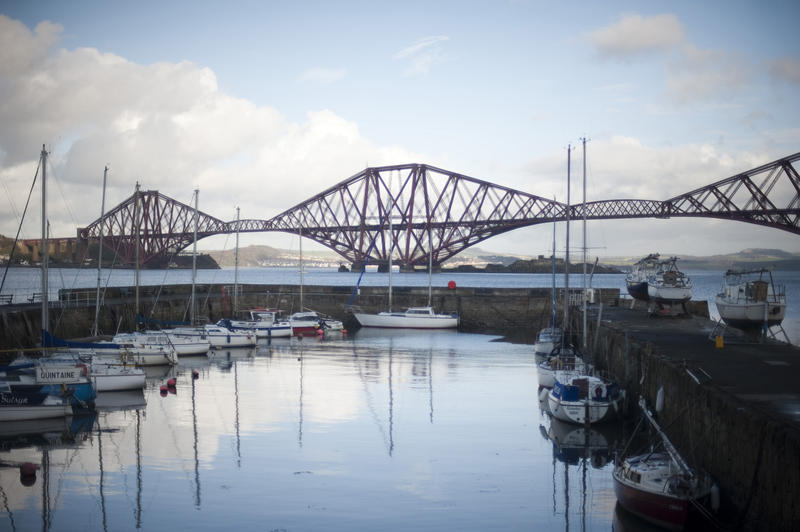 Small pleasure craft and yachts moored in the sheltered water of the Queensferry harbour with the Forth Rail Bridge silhouetted against the skyline