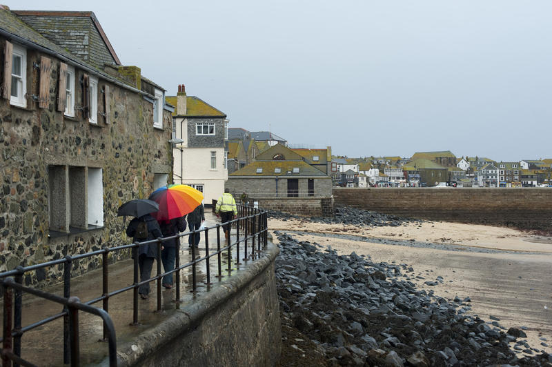 Rainy day at St Ives, Cornwall with people huddled under umbrellas hurrying along a waterfront walkway above the harbour