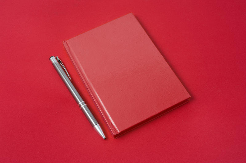 Overhead view of a closed red diary and pen lying on a red background