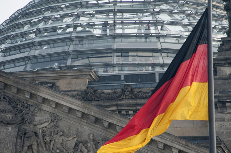 The German National flag flying in front of the glass dome of the Reichstag building and the German parliament