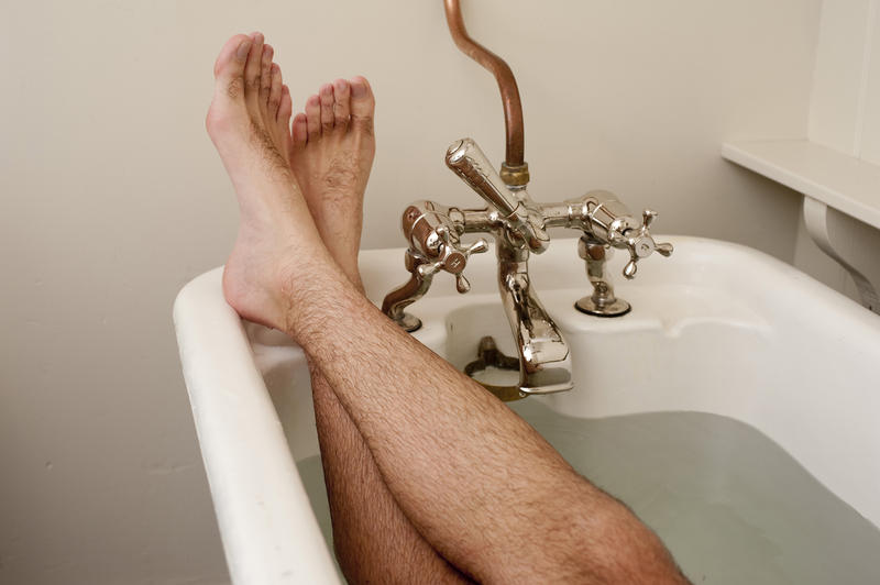 Crossed male feet in a relaxing position in a bathtub with old-fashioned faucet