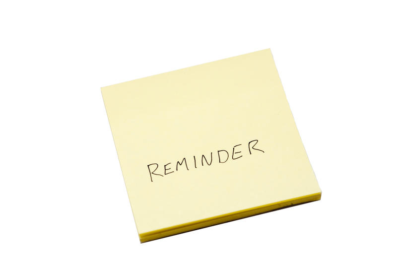 Handwritten reminder note on a square yellow notepad of sticky notelets