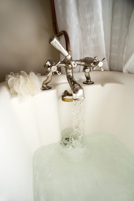 Closeup of a retro combination metal tap fitting with hot water flowing while running a relaxing bath
