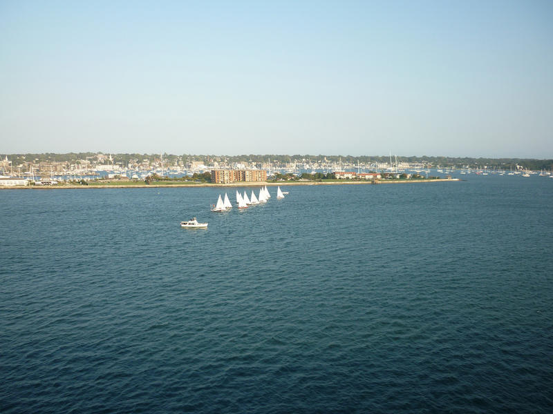 Group of small pleasure yachts out sailing close together possibly participating in an offshore race with an urban coastline in the distance