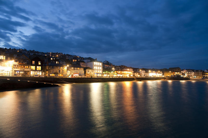 Twilight view of St Ives, Cornwall, waterfront with bright colourful lights reflected in the calm water of the harbour