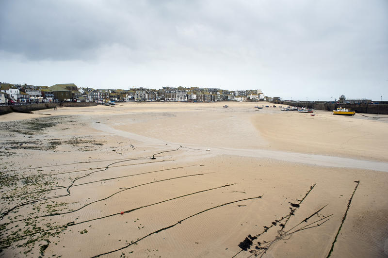 Saint Ives, Cornwall at low tide with the mooring lines of small fishing boats stretched out on the sand and the waterfront buildings visible in the distance surrounding the harbour