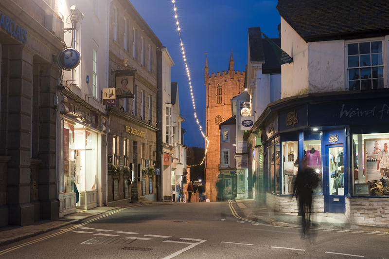 Street scene in St Ives, Cornwall at night with illuminated shops and a single blurred pedestrian