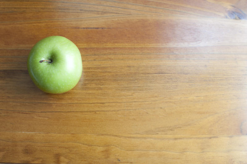 A single green apple on a wooden school desk background, with space for your text