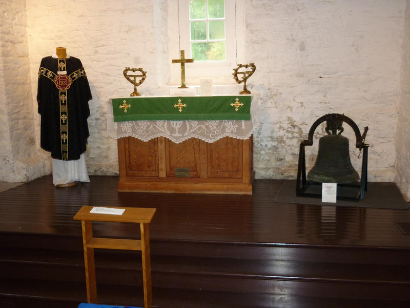 Small simple altar in a rustic church or chapel with a priests robes and bronze bell on display flanking the altar
