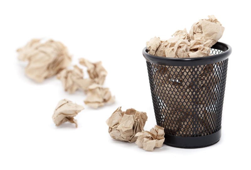Wastepaper basket filled with crumpled paper which is overflowing onto the floor alongside it