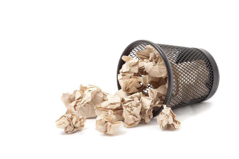 Crumpled waste paper spilling out of a bin onto the floor on a white background