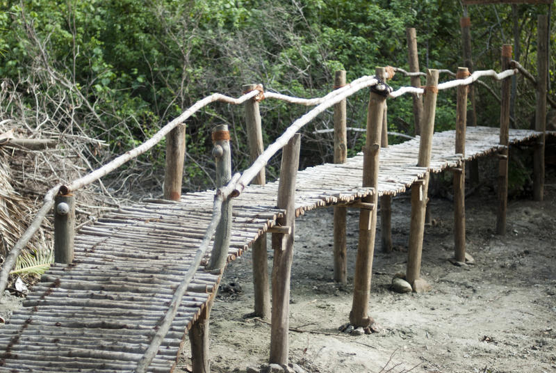 Rustic wooden pedestrian bridge constructed of elevated rough logs and poles spanning a dry creek