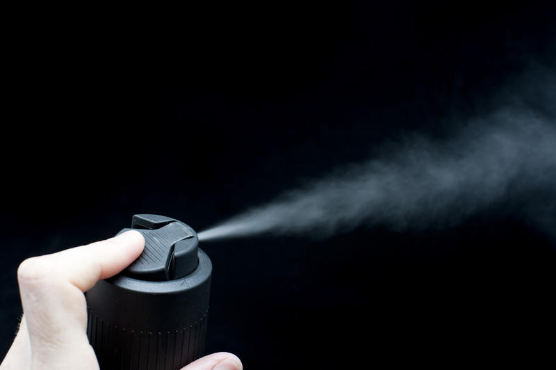 Cropped view of a male finger depressing the nozzle and spraying liquid from a spray can with the fine mist visible over a black background