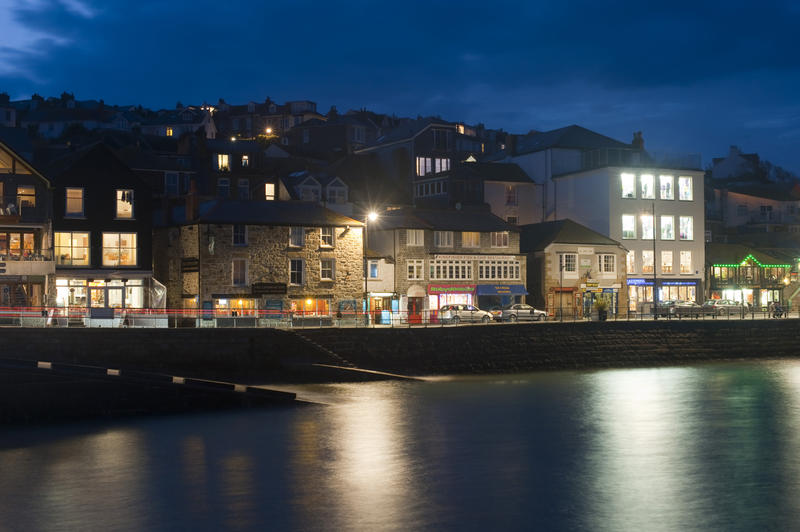 Looking from the water to the harbour of St Ives, Cornwall, showing illuminated buildings at night time with the light reflected in the calm harbour basin