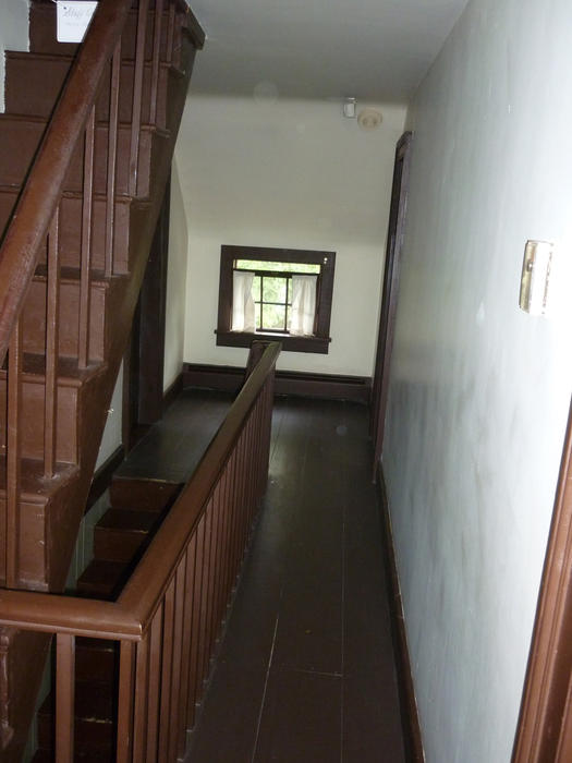Wooden staircase and floorboard landing in an old, empty house, looking towards small window