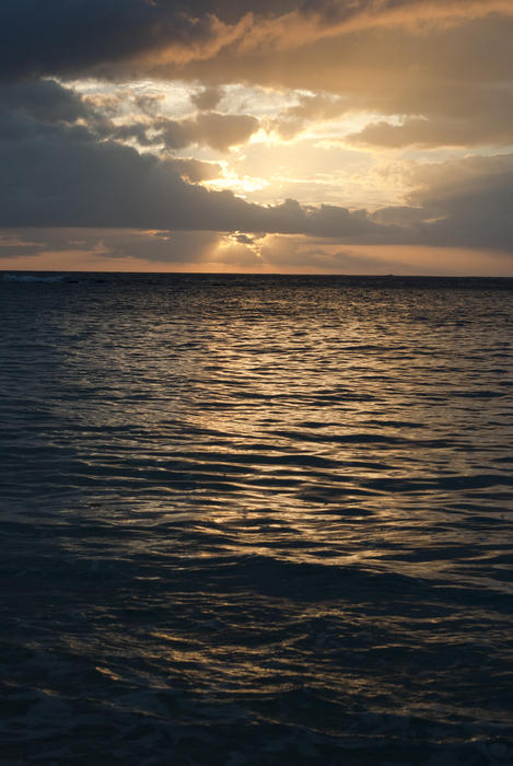 Glowing sunset over the ocean breaking through cloud cover casting an orange reflection across the surface of the water