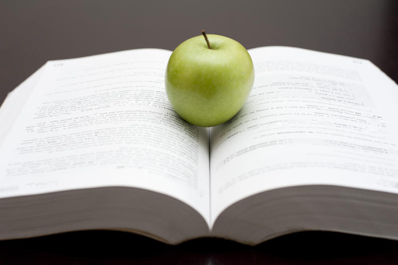 Closeup of a large open textbook with a fresh green apple balanced between the pages for a healthy snack while studying