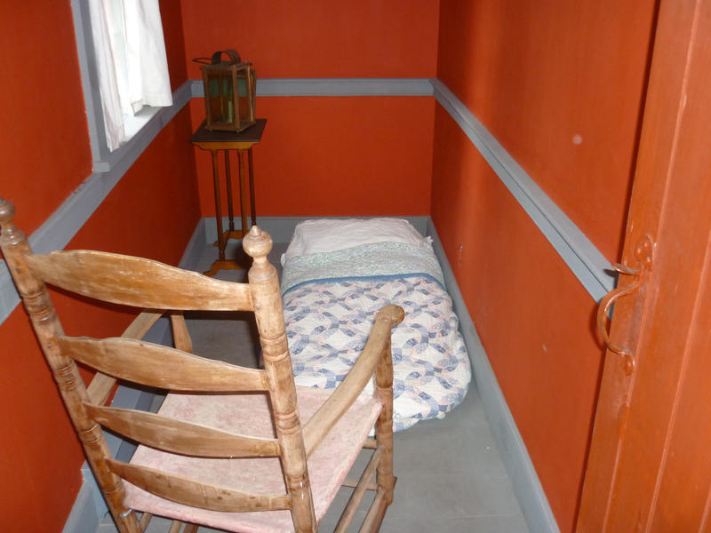 Very tiny bedroom interior with room for a single pallet on the floor to sleep on and a single wooden rustic chair