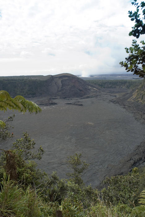 Solidified lava forms a flat surface in the Kilauea Iki Crater, Hawaii Volcanoes National Park, steam from the Kikauea Caldera crater can be seen to the rear