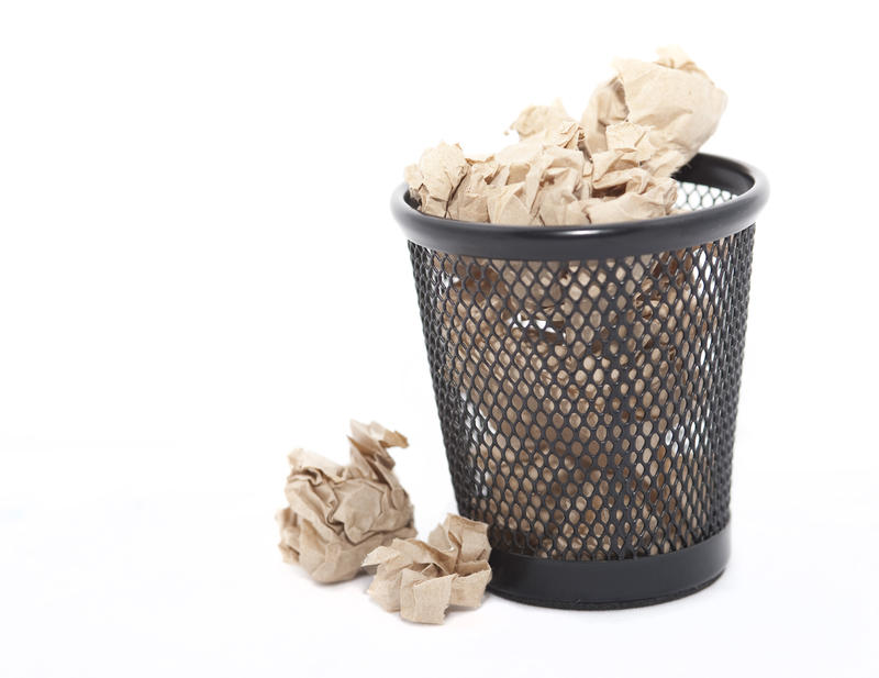 Crumpled waste paper in a bin which is full and overflowing on to the floor