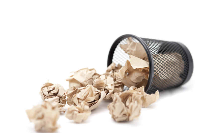 Untidy wastepaper basket lying on its side with crumpled paper spilling out onto the floor