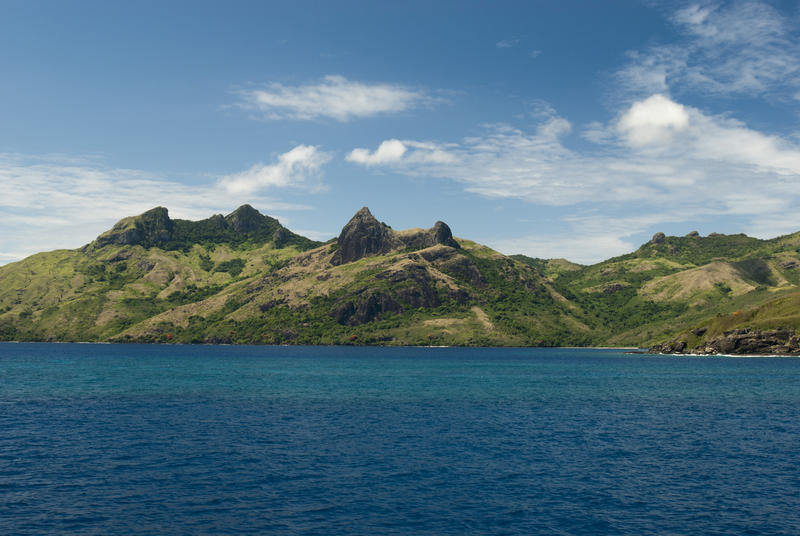 A view of Waya Island, Fiji from the ocean showing its rocky hilly terrain and golden beaches, a perfect tropical vacation getaway