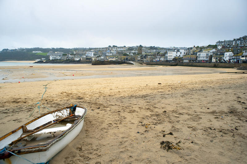 View across a sandy beach with a small wooden dinghy in the foreground of the popular fishing town of Saint Ives, Cornwall