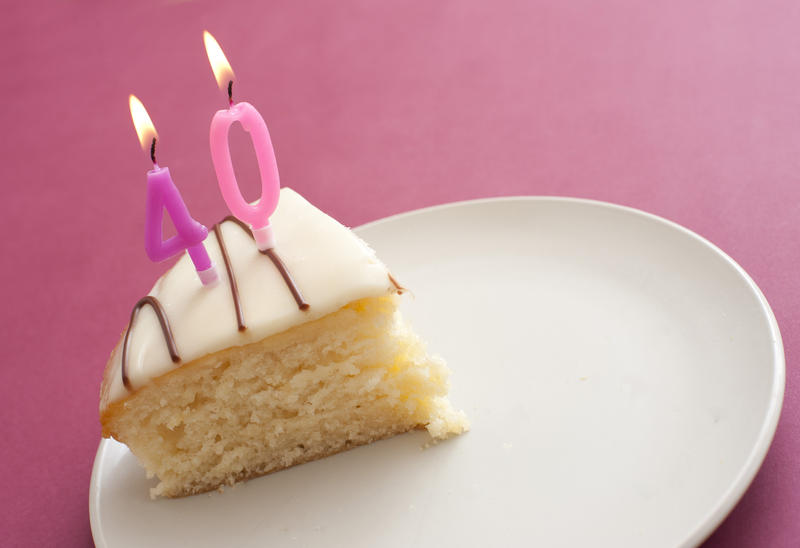 Slice of 40th birthday cake with burning pink number candles denoting the age served on a plate on a pink background for a woman, with copyspace