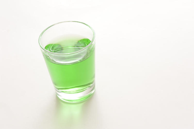 Glass of green absinthe liqueur, a potent beverage with a high alcohol content made with herbs, anise and wormwood, on a white background with copyspace