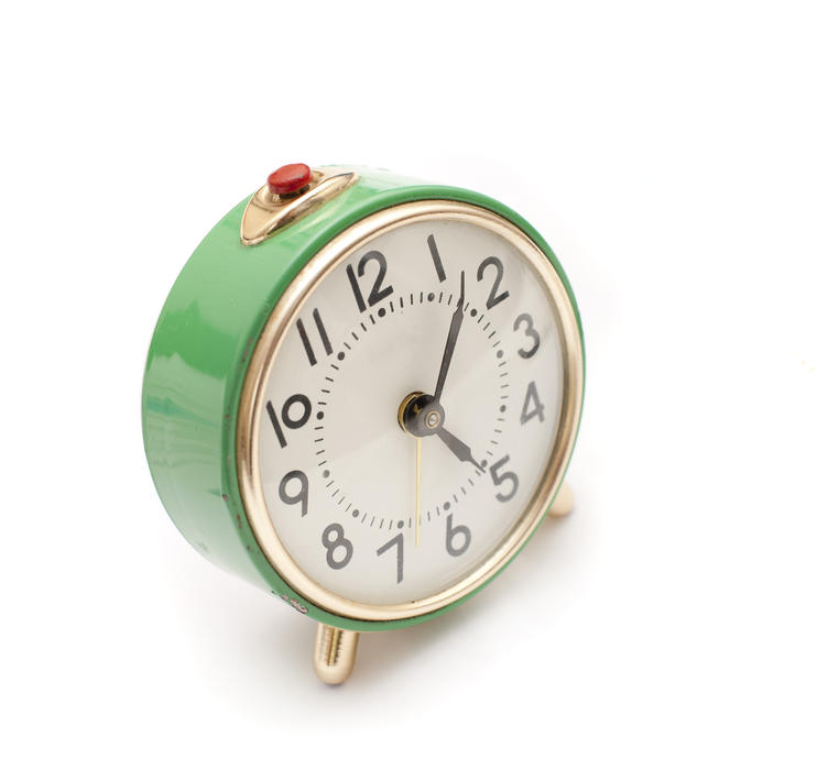 Round green metal alarm clock with a red button to deactivate the ring at the top and Arabic numerals on a white background