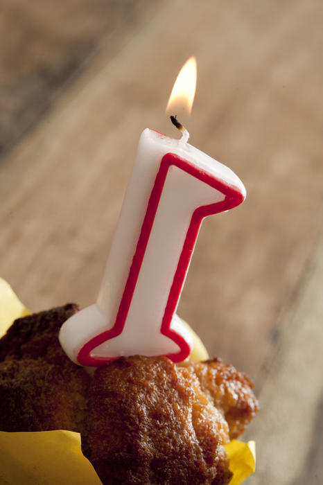 First anniversary celebration concept with a burning number one candle on a freshly baked muffin, close up high angle view