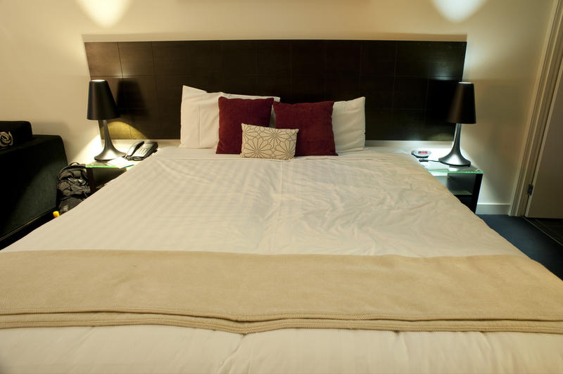 Double bed with a dark headboard flanked by modern lamps and stacked cushions in an apartment bedroom