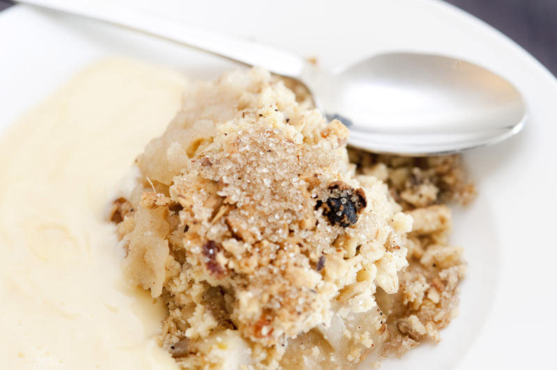 Close up of a serving of delicious spicy apple crumble and custard in a bowl with a spoon
