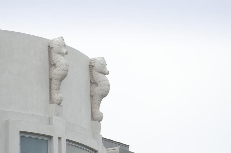 Art Deco ornamentation in the form of two white sea horses on the exterior wall of a building against a cloudy blue sky with copyspace
