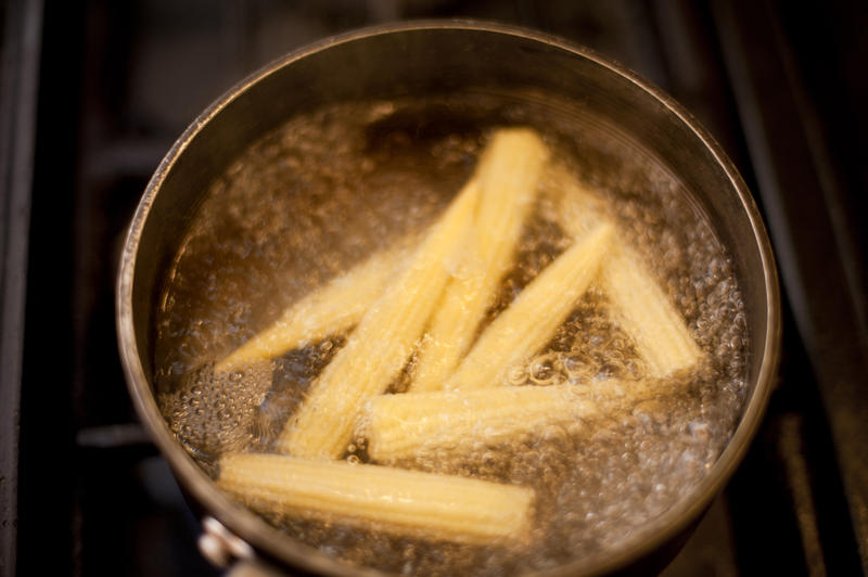 Baby sweetcorn boiling in a pot or saucepan on a hob, high angle view of the corn and bubbling water