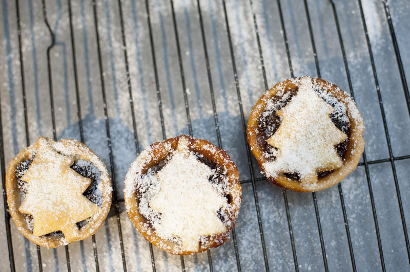 Three fruity traditional Christmas mince pies on a cooling rack in the kitchen, overhead view with copyspace