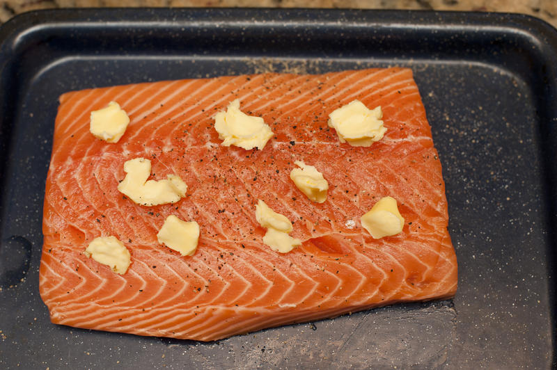 Close up Slice of Baked Salmon with Butter on Top for Dinner Served on a Black Tray