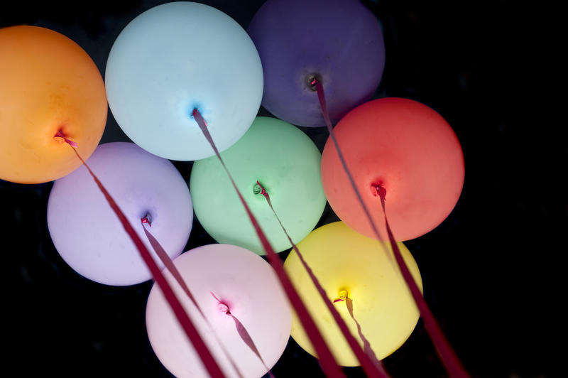 Colorful party balloons in the colors of the spectrum tied with ribbons floating high in the air above on a black background depicting a festival birthday, anniversary or holiday celebration