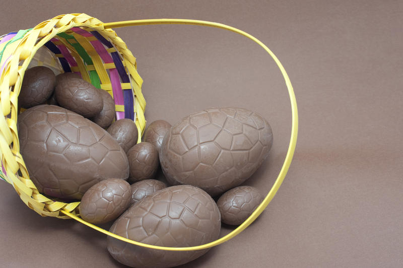 Basketful of chocolate Easter Eggs lying on its side with several eggs spilling out onto the brown background