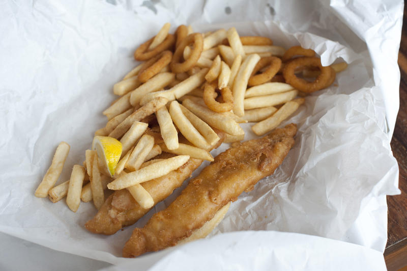Takeaway meal of deep fried battered fish and chips served on a crumpled piece of white paper packaging