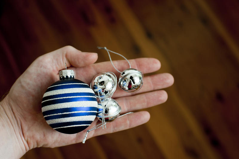 Man holding silver bells and a colorful blue striped Christmas bauble in his hand displaying them to the camera over a dark background