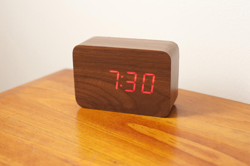 Close up Dark Brown Wooden Bedside Led Clock on Top of Wooden Table with White Wall Background.