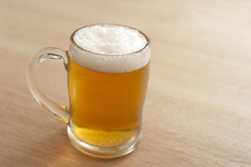 Glass mug or tankard of cold frothy beer standing on a wooden table in a bar or pub, high angle view