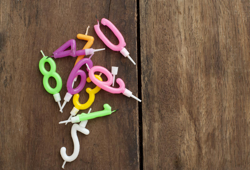 Jumble of colorful Birthday candles with number 0 through 9 lying on a rustic wooden background with copyspace