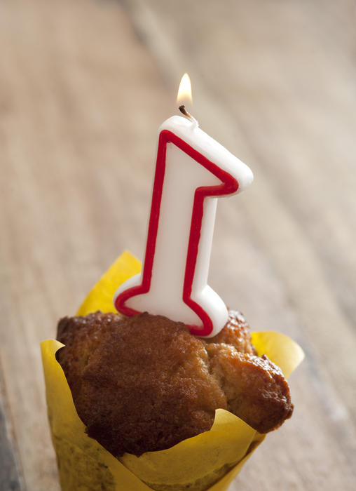 First birthday decorative cupcake with a burning number one candle to celebrate the birthday of a baby, high angle over a wooden background