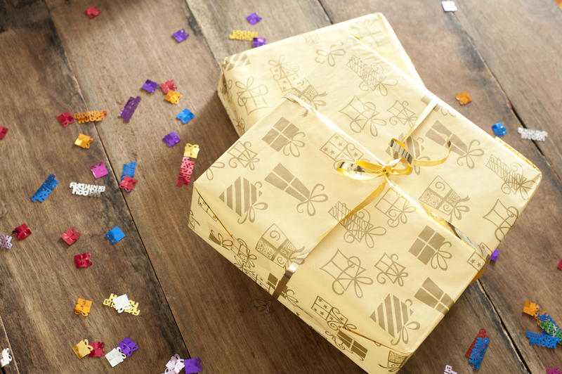 Two decorative gift-wrapped birthday presents piled on top of one another on a wooden table surrounded by scattered colorful sprinkles, high angle view