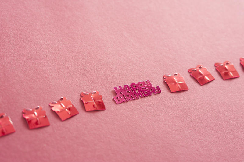 Happy birthday background for a girl with decorative cutout shapes of gifts and Happy Birthday text arranged in a diagonal line over a pink background with copyspace