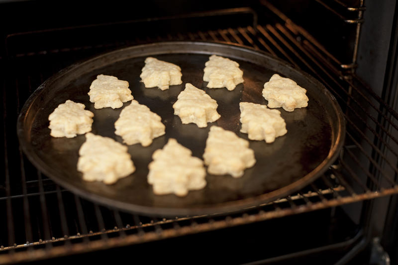 Christmas cookies in the shape of traditional Christmas trees arranged on a baking tray cooking in the oven