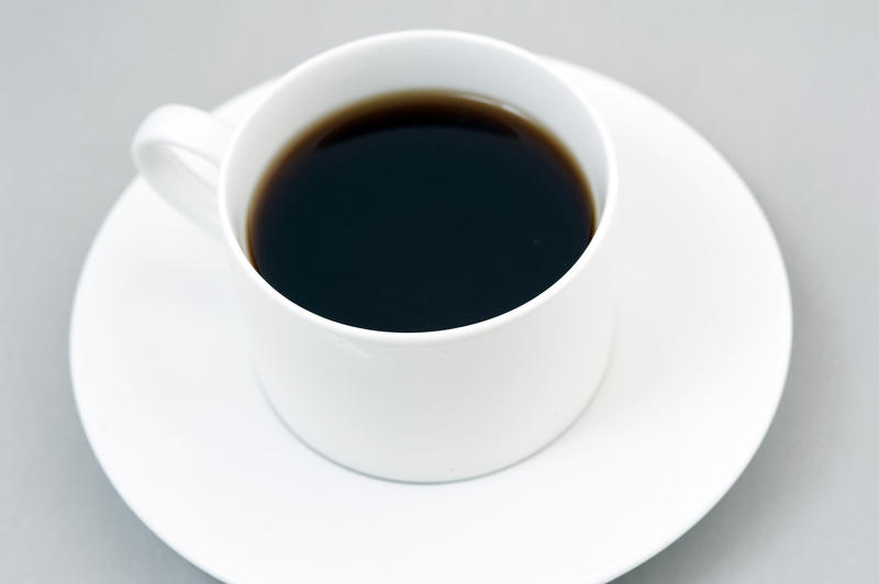 Cup of black espresso on white saucer. Grey background